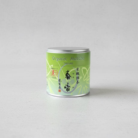 A green cylindrical can labeled 'Organic Matcha Haruka' on a wooden surface.